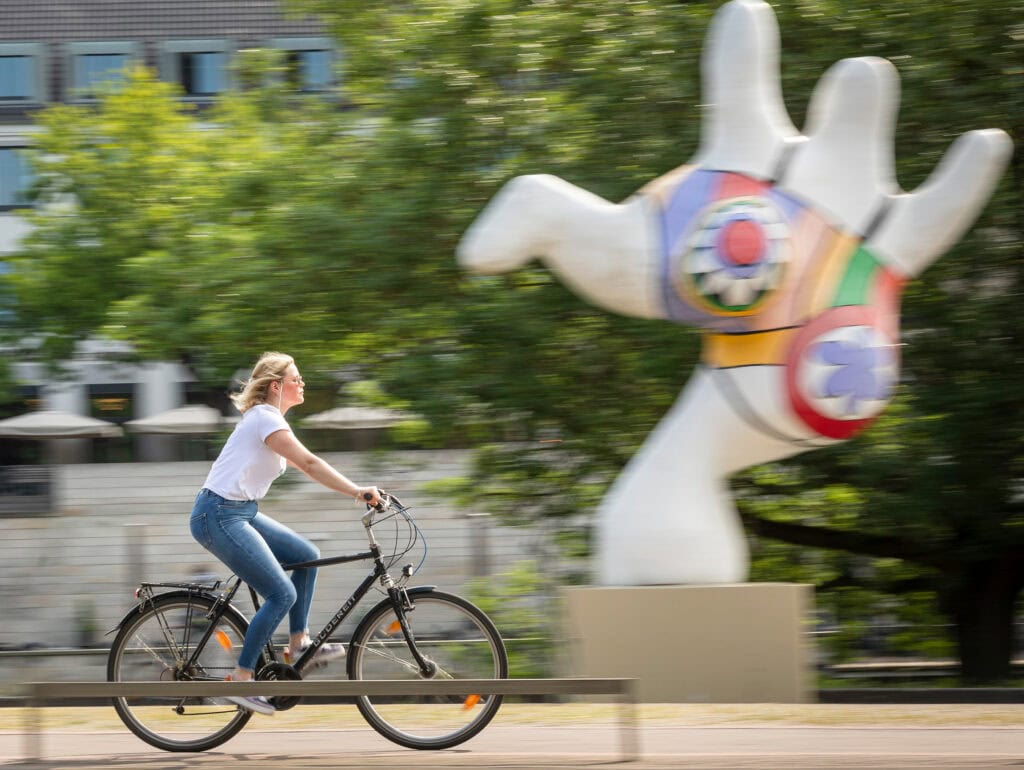 Eine junge Frau fährt mit dem Fahrrad entlang der Nanas am Leibnitzufer.